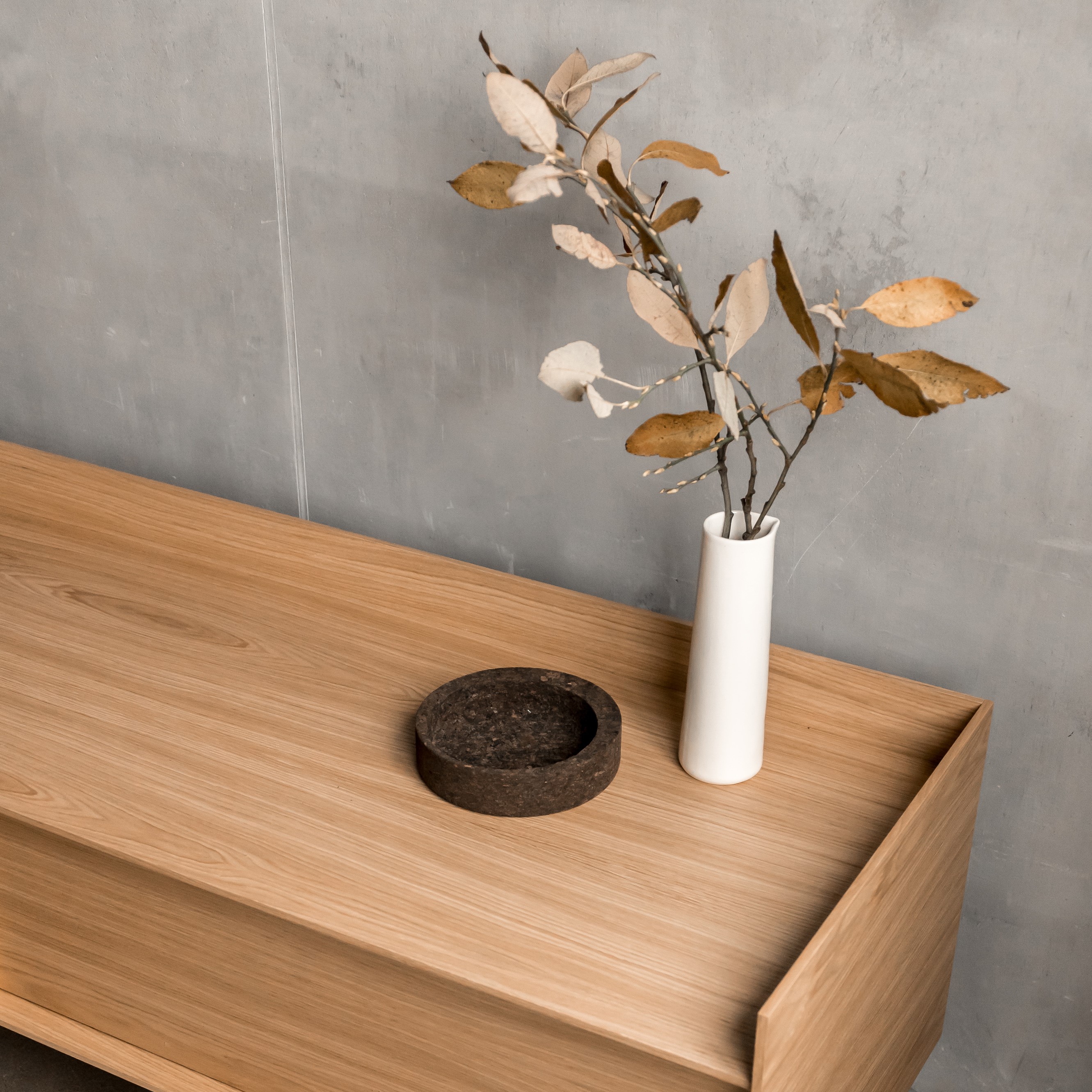 Minimalist wooden cabinet with cork tray and ceramic vase on it